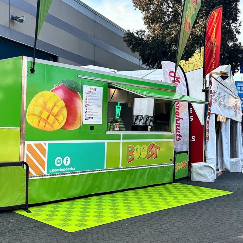 The Boost Juice trailer from the front corner, the ULTRAGRID Electric Green mat with ULTRAEDGE ramps along its edge