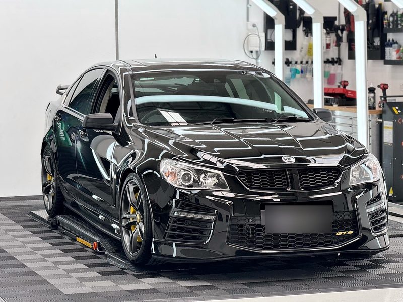 Black car beside the detailing product wall at Elite Car Detailing Studio, on an ULTRAGRID floor in Jet Black and Space Grey
