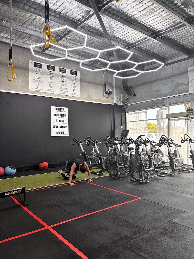 ULTRABEAM hexagon LED lights above the bike row at Tailored Fitness, a member stretching on the floor below
