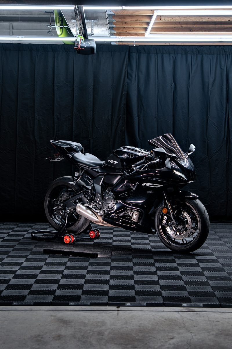 A black sportbike under the lit ceiling on the Jet Black ULTRAGRID chequer, black curtains behind