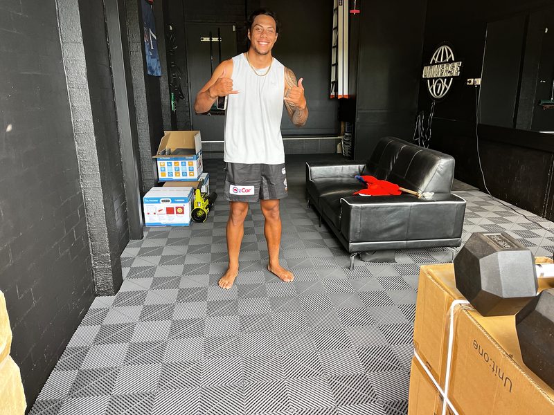 Jarome Luai standing barefoot on the finished Space Grey ULTRAGRID floor, giving two thumbs up