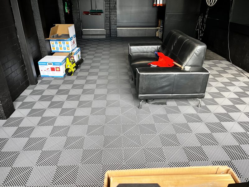 A Space Grey ULTRAGRID garage floor, finished, in a black-walled garage with a leather couch, Sydney