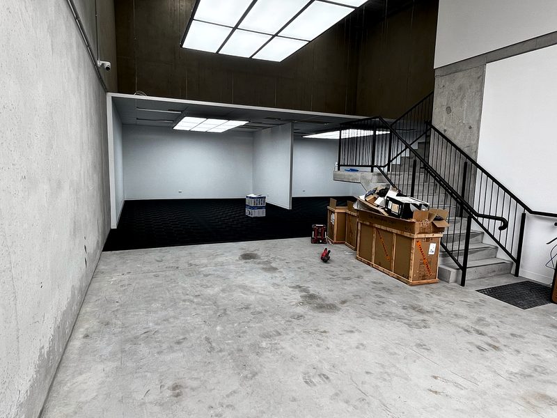 The F90 Auto Detailing unit from the entrance: bare slab in front, the Jet Black ULTRAGRID floor in the rooms beyond, stairs at right