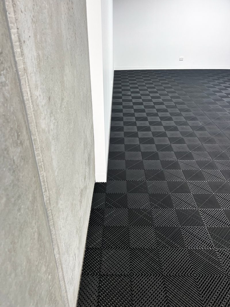 Jet Black ULTRAGRID floor running along a concrete wall panel to a white wall