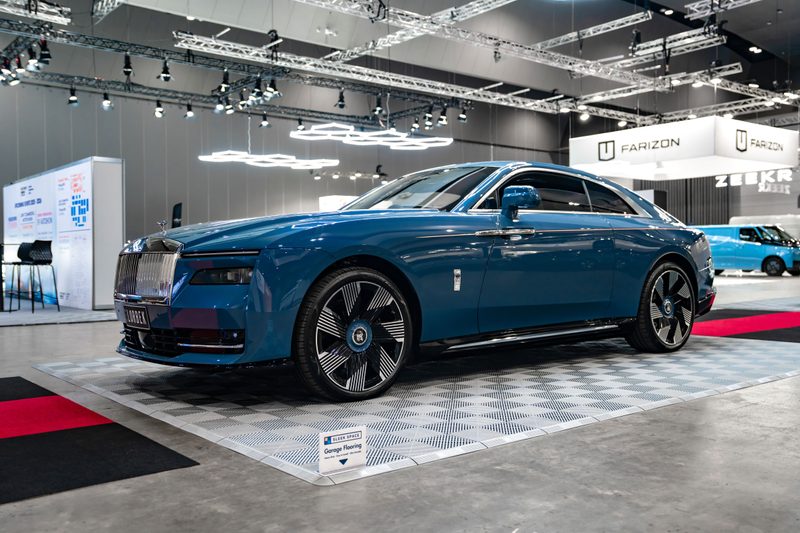 Rolls-Royce Spectre on ULTRAGRID Silver Grey tiles with a Sleek Space sign at the corner of the pad and ULTRABEAM lights above